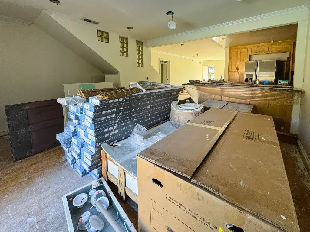 Kitchen and living area under renovation with flooring boxes, tools, and materials stacked across the room.