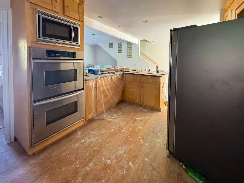 Kitchen remodel in progress with stainless steel appliances, wood cabinets, and countertops covered in plastic.